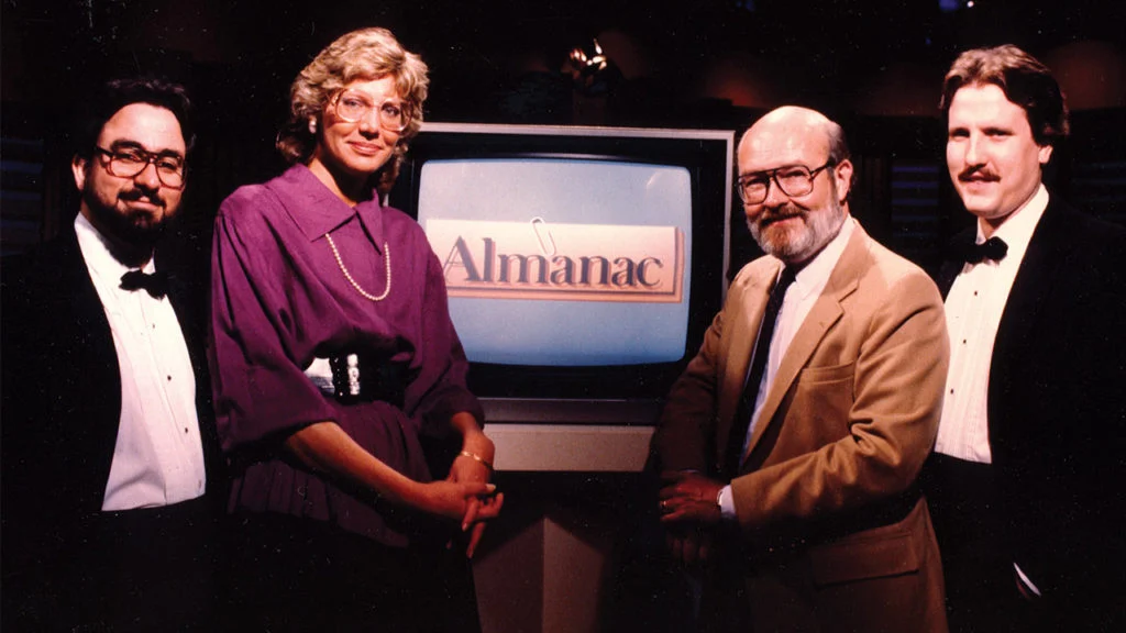 four adults standing next to 1980s TV set displaying the logo for Almanac from Twin Cities PBS